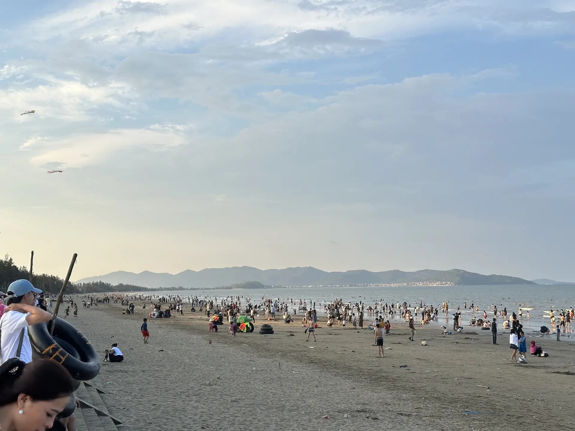Bãi biển Quỳnh Bảng đông người tắm chiều, phía xa là dãy núi