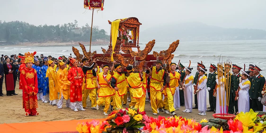 Lễ rước kiệu trong lễ hội đền Cờn diễn ra ngay trên bãi biển: đoàn người mặc áo tế vàng và đỏ khiêng kiệu sơn son thếp vàng đi trên cát, hai bên là hàng người cầm hương và cờ, phía sau là sóng biển