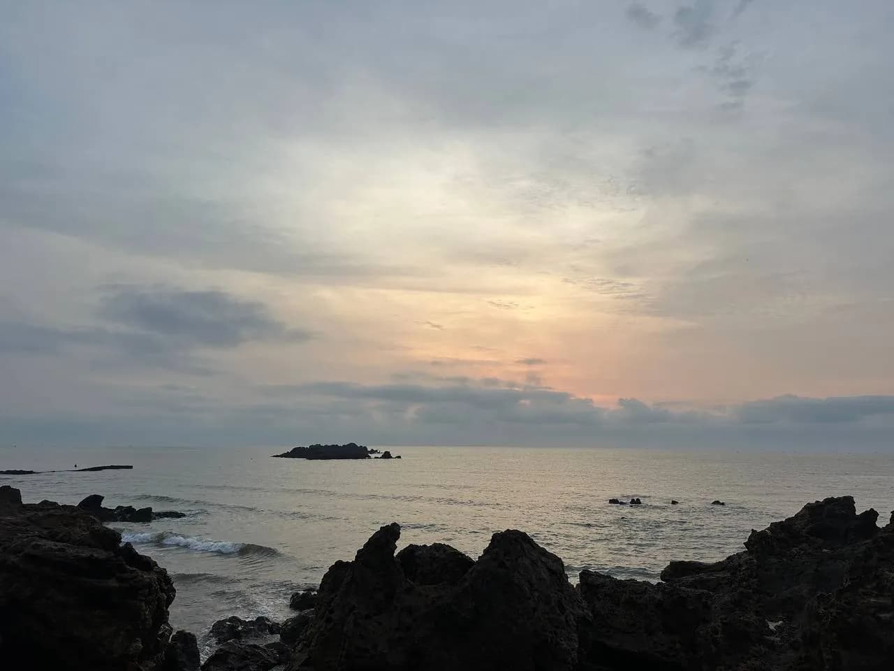 Bờ đá bãi Quỳnh Lương lúc trời ngả vàng, một hòn đá nhỏ nổi giữa mặt nước lặng ngoài khơi