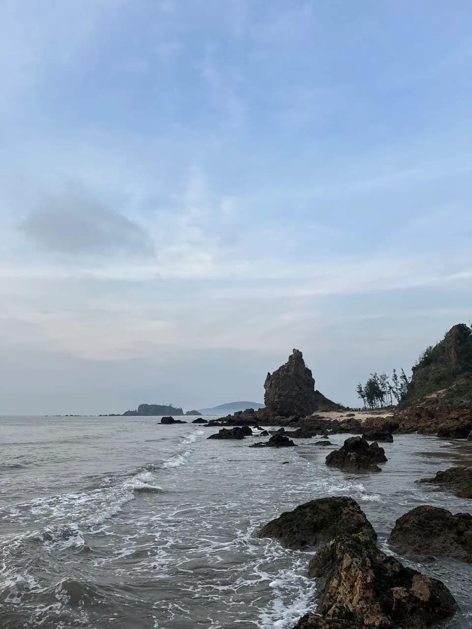 Mỏm đá cao nhô lên giữa bờ đá bãi Quỳnh Lương, hàng phi lao trên đồi và mấy hòn đảo mờ phía chân trời